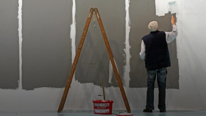 Ein älterer Herr mit grauen Haaren weißt eine Wand