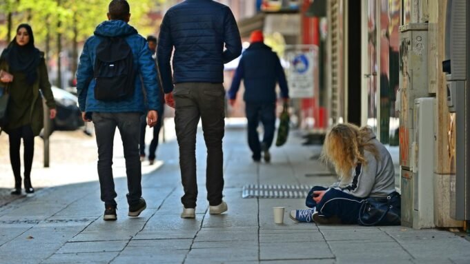 Obdachlose Frau in der Frankfurter Innenstadt, Passanten laufen an der Frau und ihrem Pappbecher in dem sie Spenden sammelt vorbei.