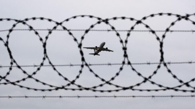 Symbolbild: Ein Flugzeug startet am Flughafen Hannover - fotografiert durch Stacheldraht am Flughafenzaun. 